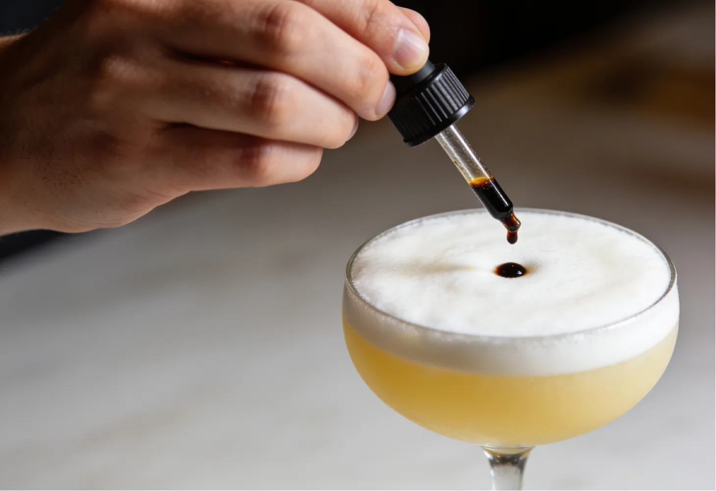 Decorando la espuma del Pisco Sour de Maracuyá con amargo de angostura